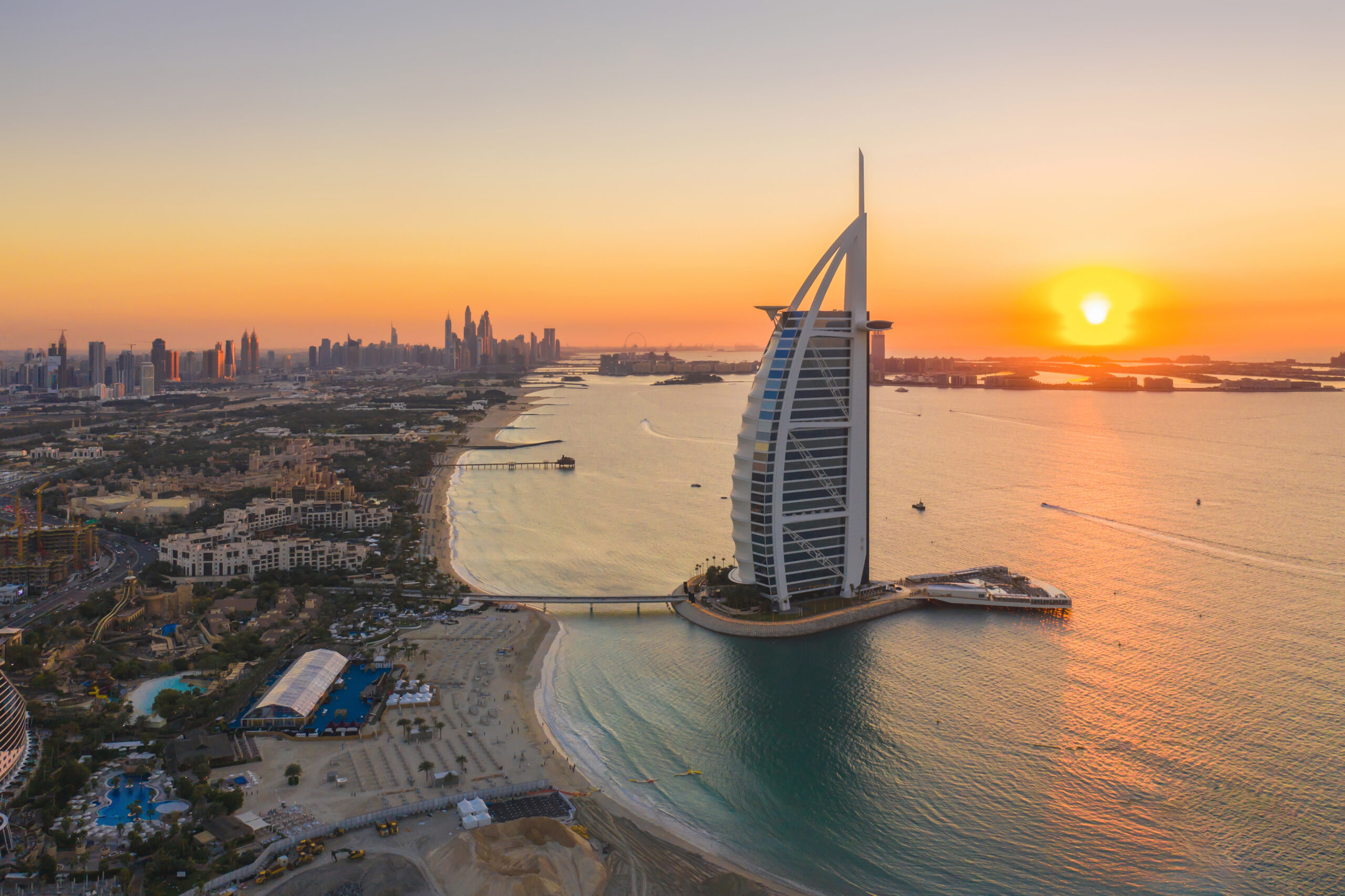 Aerial view of Burj Al Arab Jumeirah Island or boat building, Dubai Downtown skyline, United Arab Emirates or UAE. Financial district in urban city. Skyscrapers at sunset.
