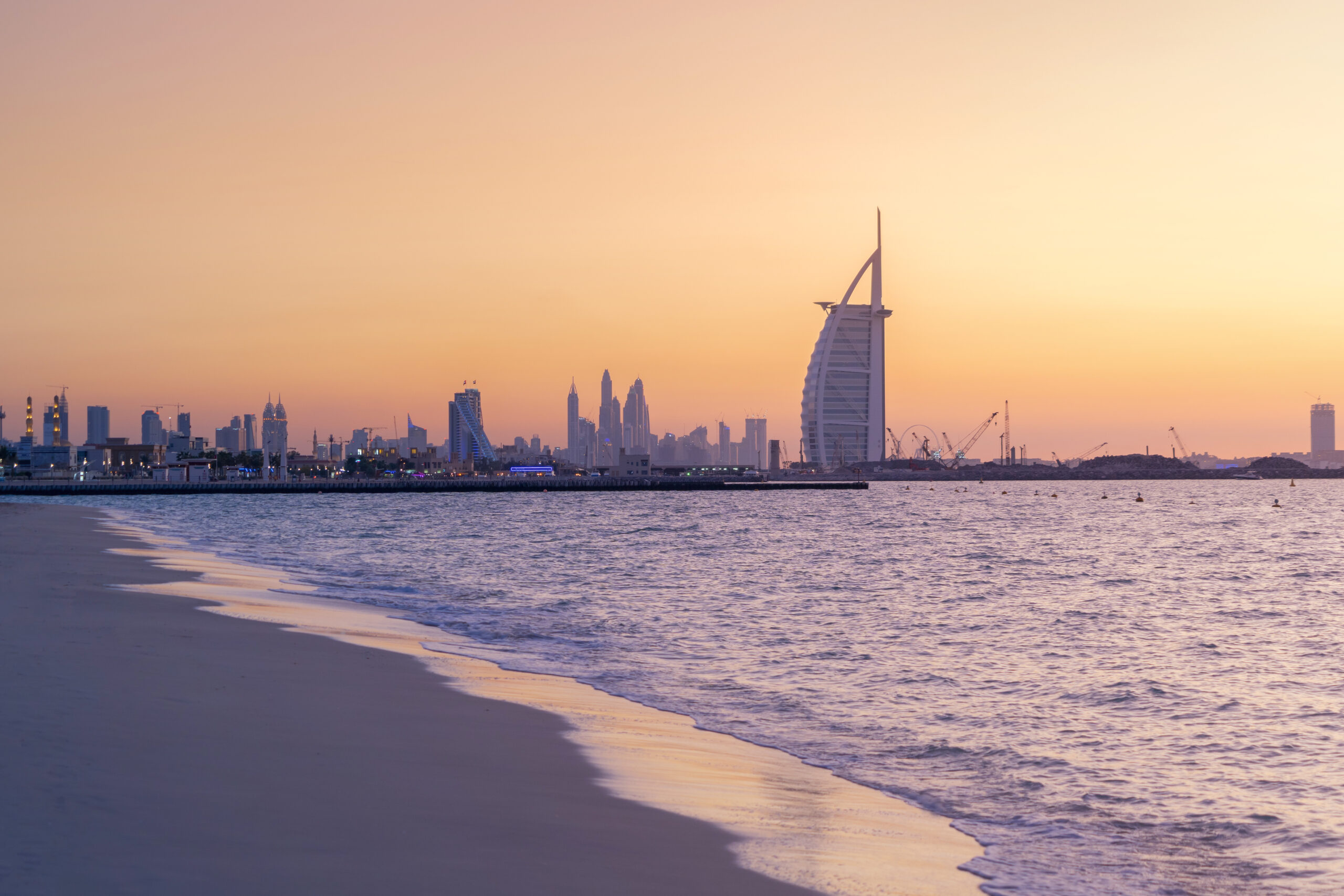 Burj Al Arab in Jumeirah Island or boat building with waves on sea beach, Dubai Downtown skyline, United Arab Emirates or UAE. Financial district in urban city. Skyscrapers at sunset.